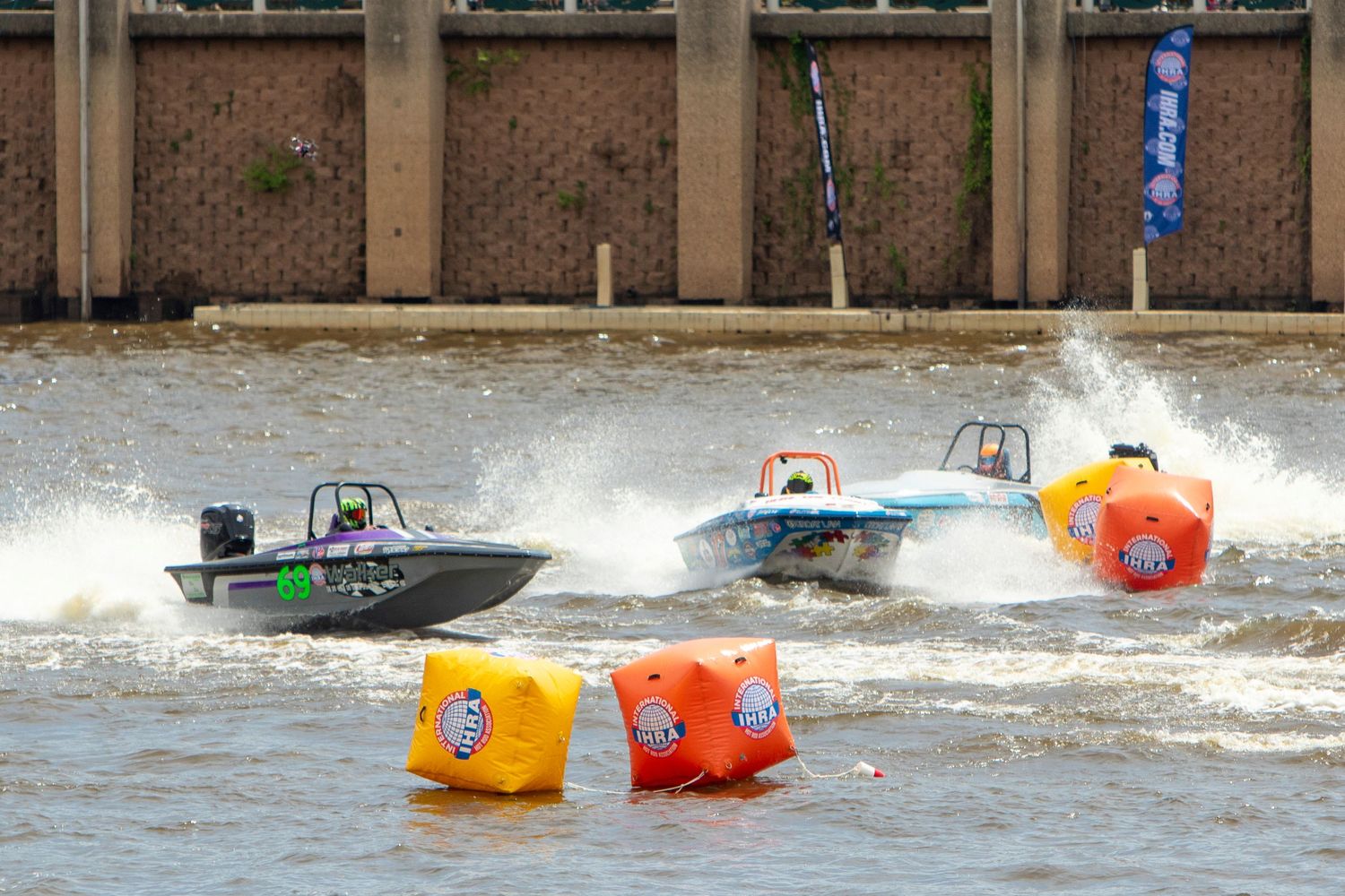 Two speedboats racing on a river course marked by colorful orange and yellow buoys during a competitive powerboat race.