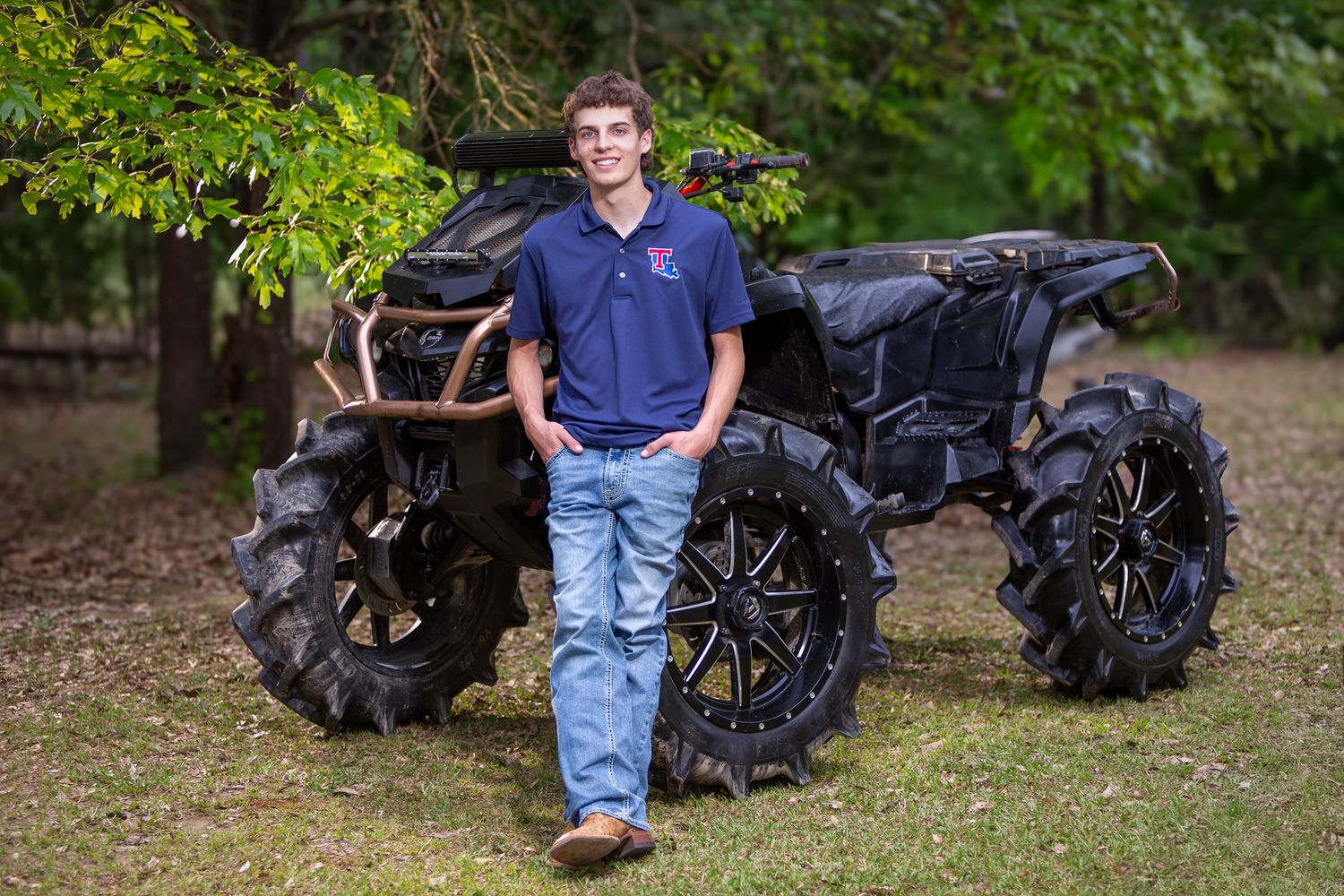 ATV with custom mud tires parked on grass with trees in background.
