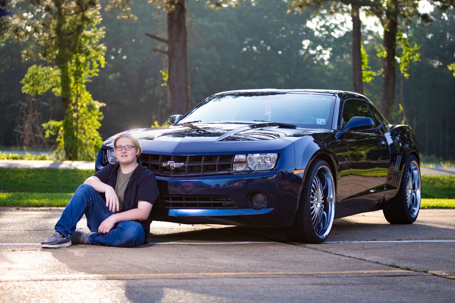 A blue sports car is photographed in multiple angles at sunset in a tree-lined parking area.