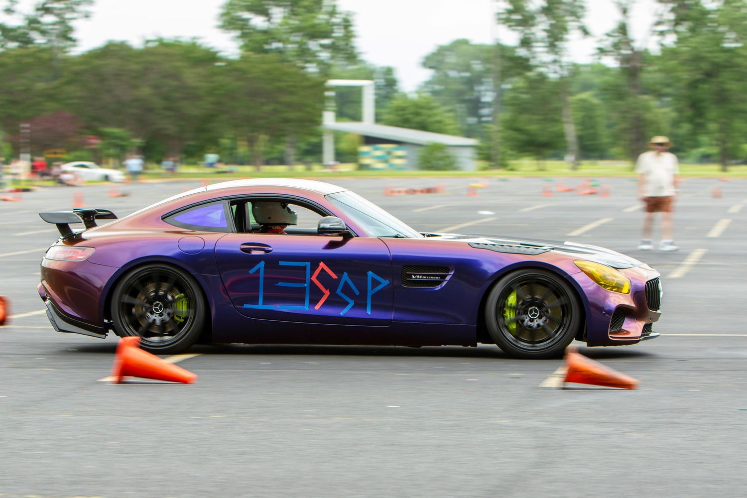 Purple Mercedes-AMG GT race car navigating orange cones on an autocross course during a motorsport event.