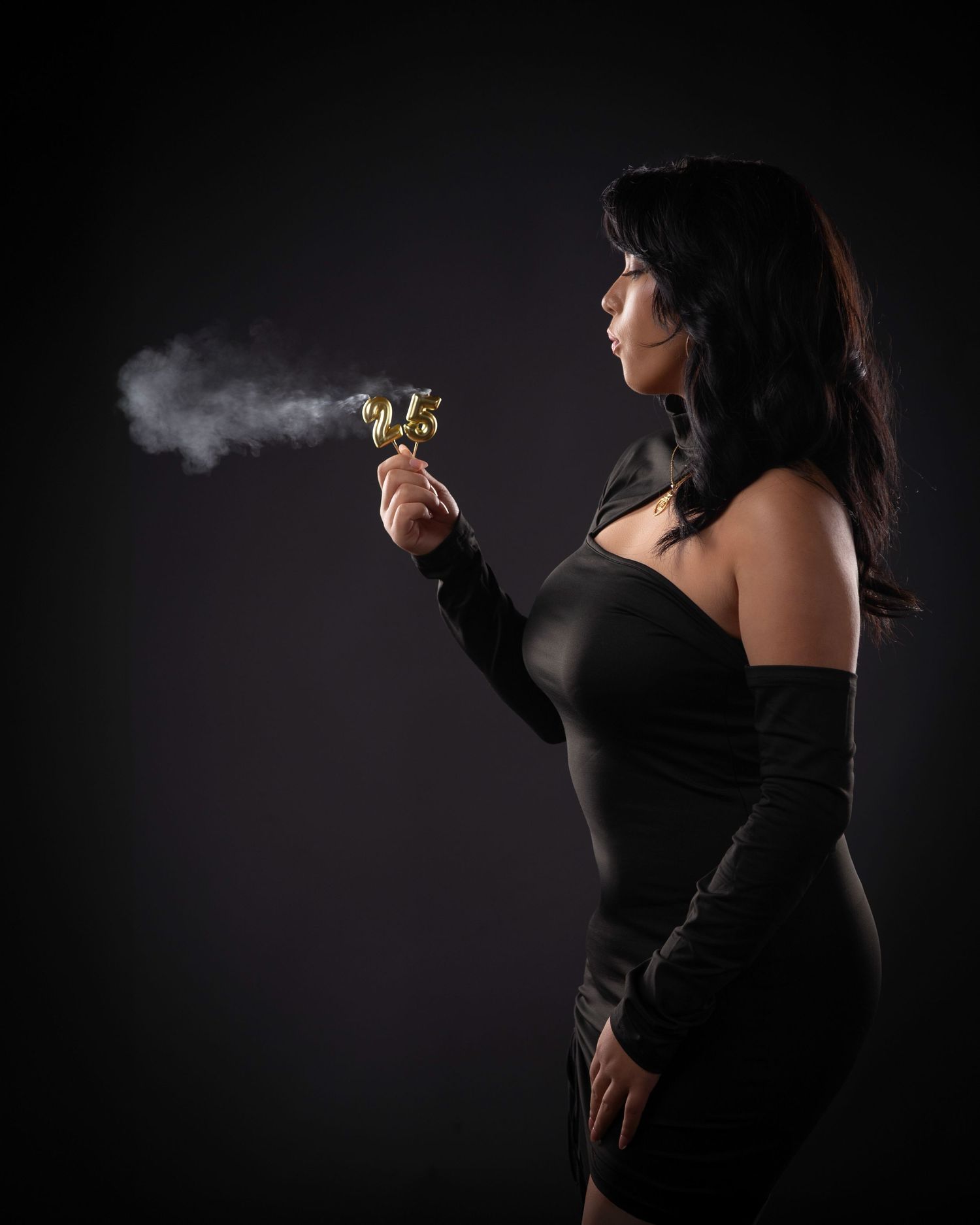 Silhouette of person in black dress blowing smoke against dark background in dramatic lighting.