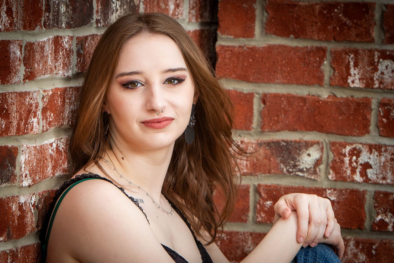 Professional high school senior portrait session against rustic brick wall background with warm lighting and natural styling.
