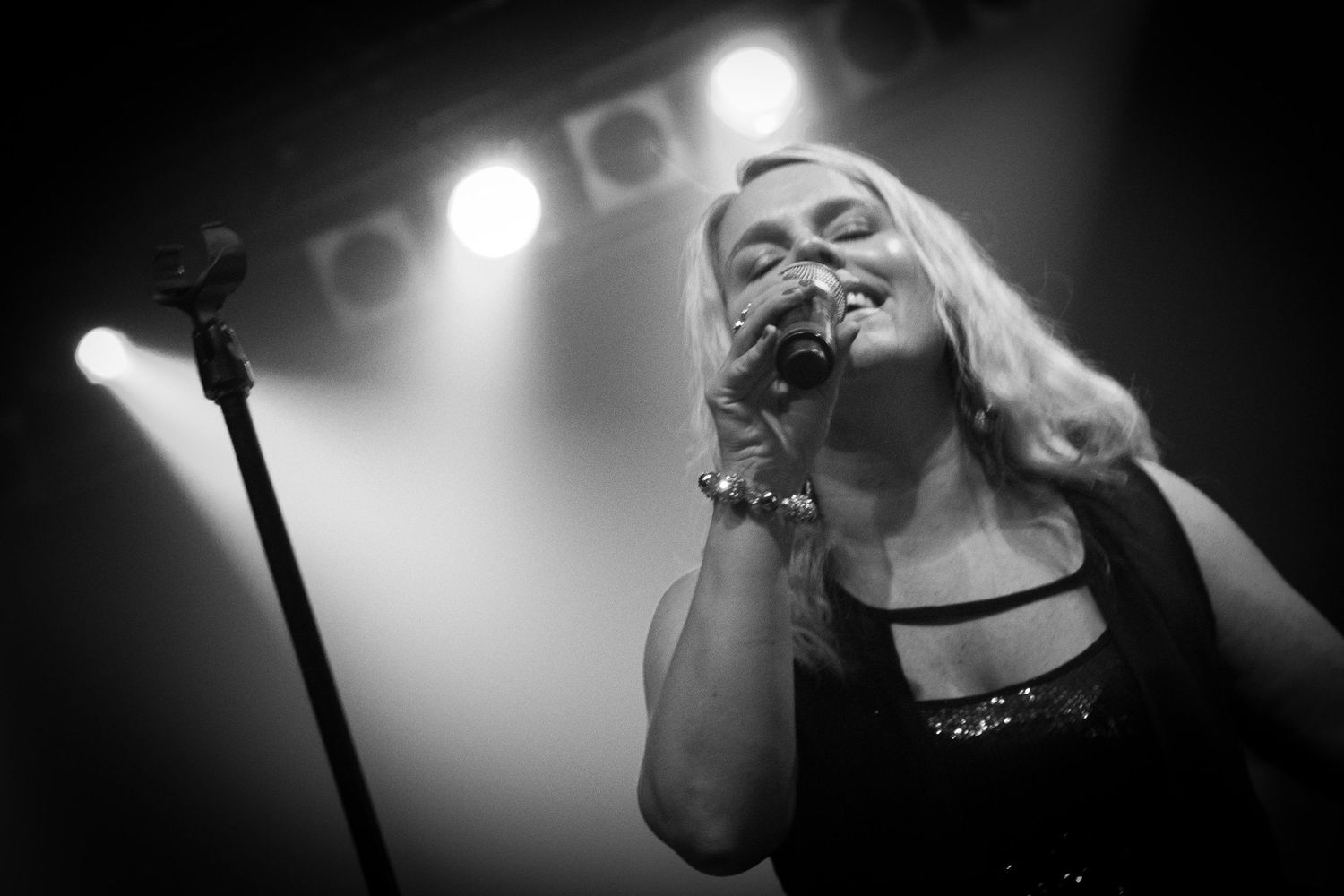 Black and white photo of a female singer performing on stage with microphone and bright spotlights behind her.