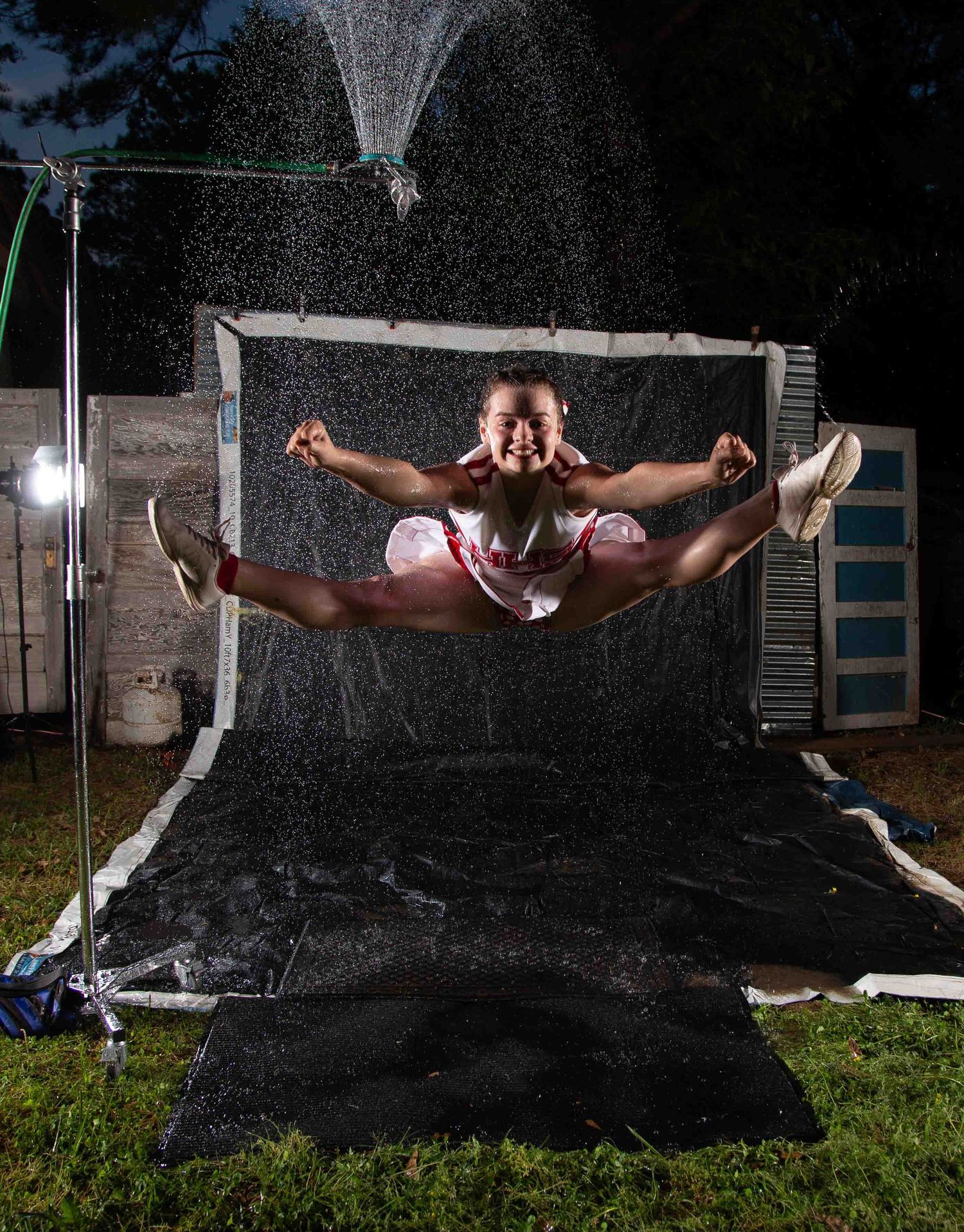 Gymnast performing a split leap jump outdoors at night with water spray backdrop and studio lighting.