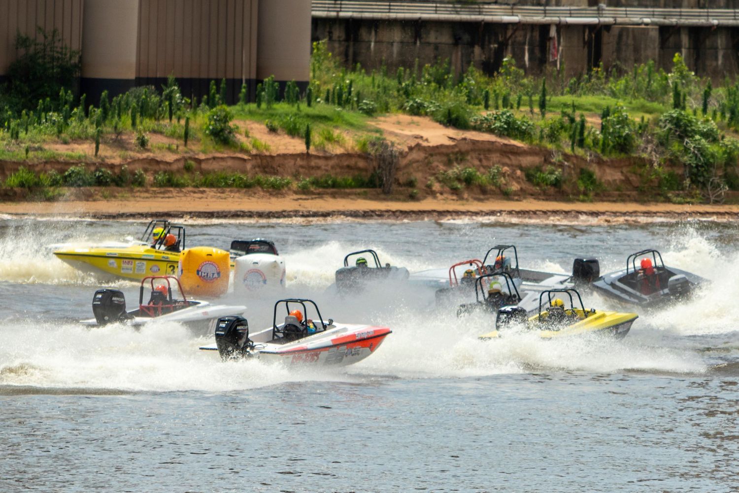 Multiple colorful speedboats racing across a river during a competitive powerboat racing event with splashing water.