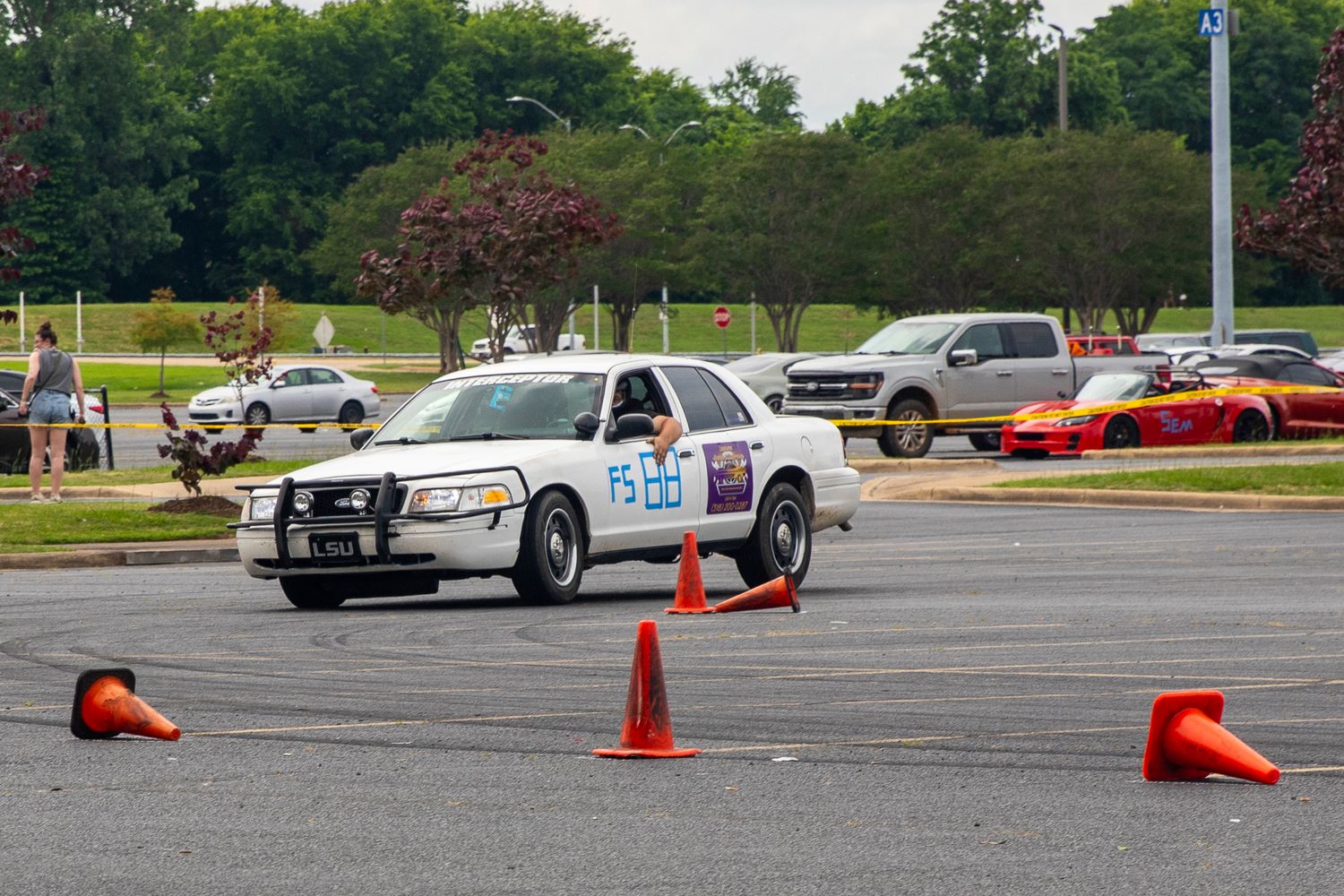 Police car navigating orange traffic cones in a parking lot autocross course during a driving skills event.