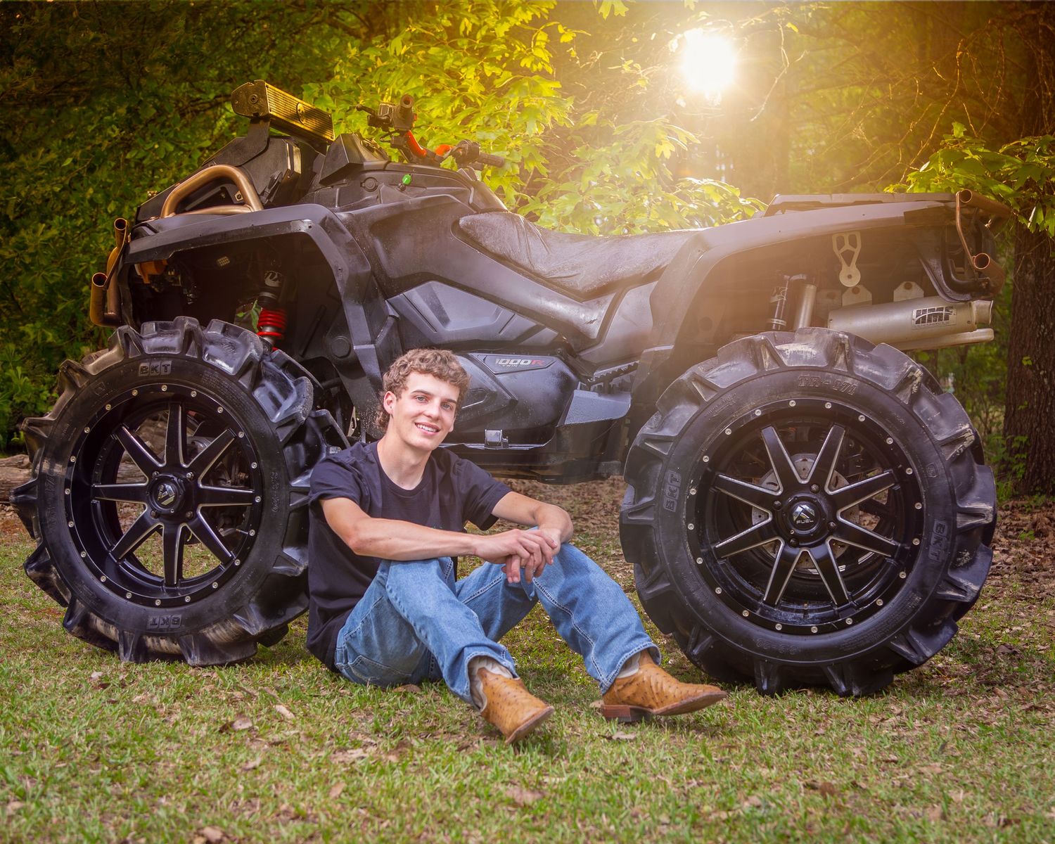 A black ATV with large off-road tires is parked on grass during golden hour sunlight.