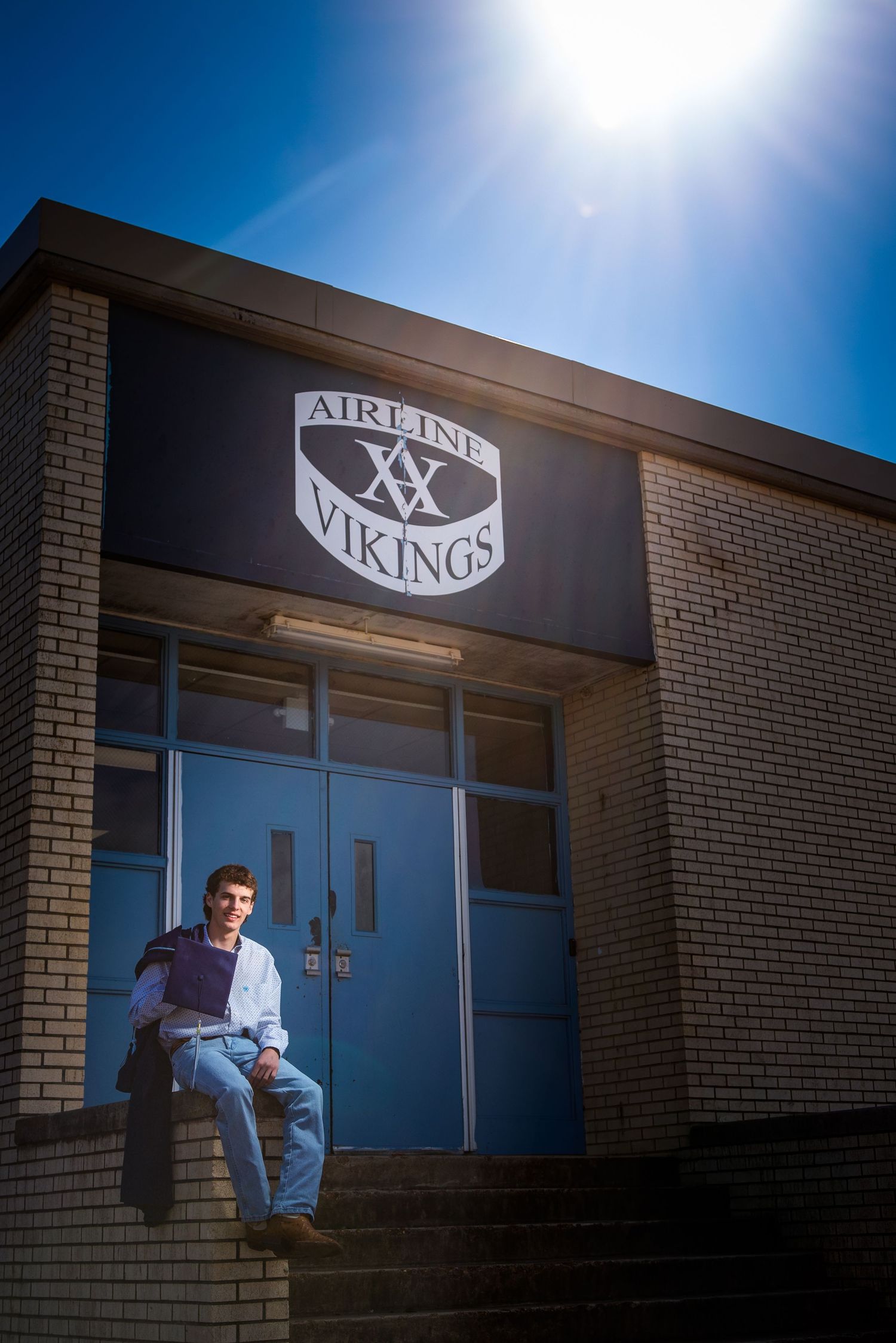 Person in casual attire stands against brick wall exterior of Vikings athletic facility under blue sky.