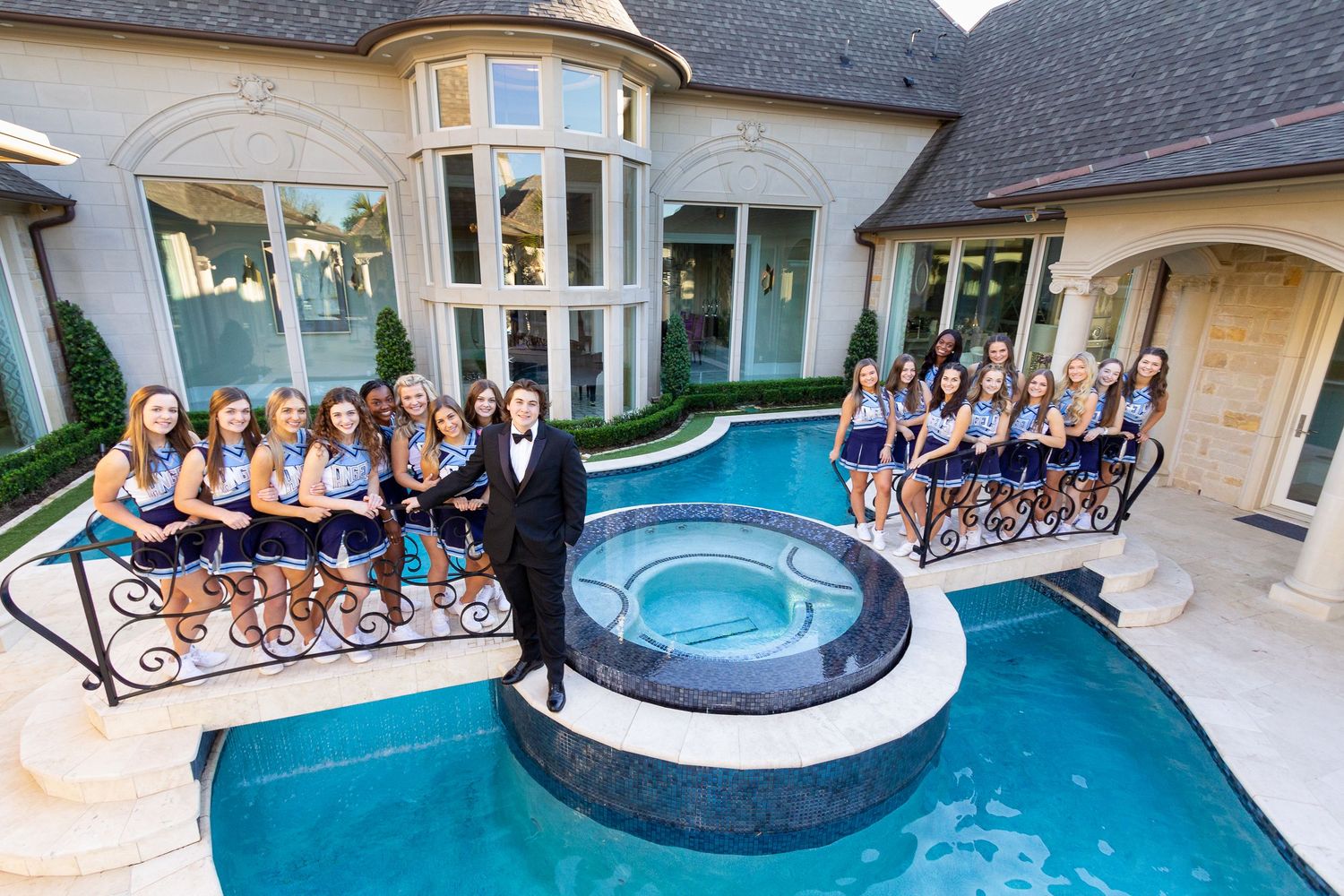 Group of bridesmaids in blue dresses posing with groom by luxury mansion pool and hot tub.