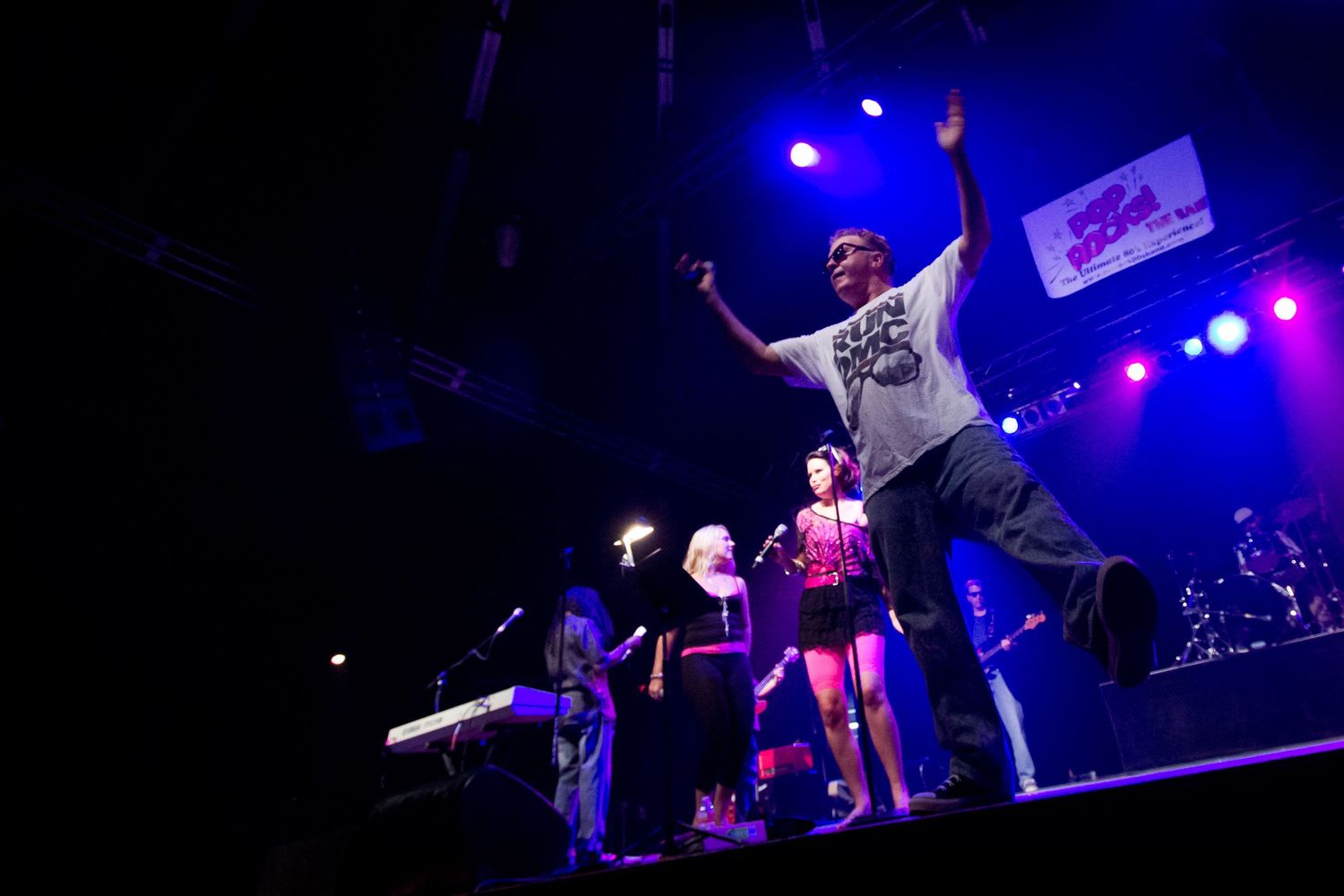 Energetic performer on stage with raised arms under colorful lights at a live music concert.