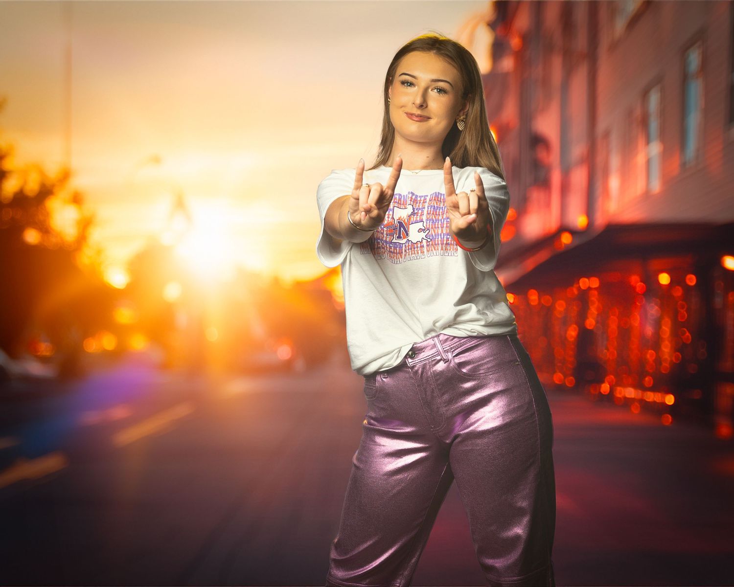 A person in metallic purple pants and white t-shirt poses on a city street at sunset with dramatic orange lighting.