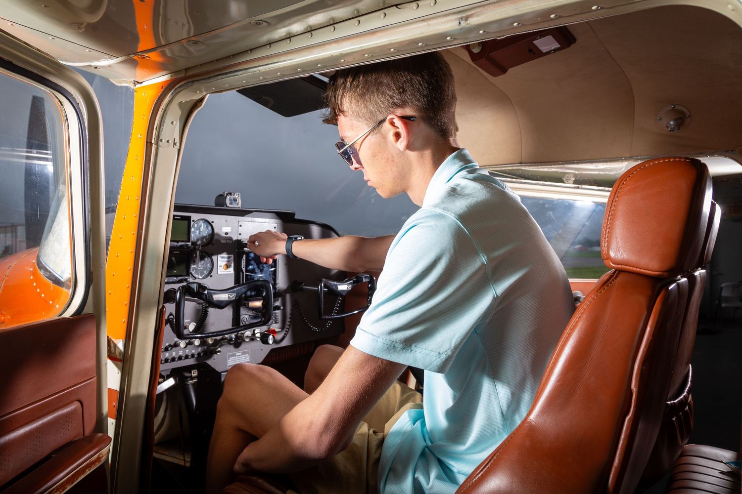 Someone in a light blue shirt installs wiring and components in a vintage orange Volkswagen van interior.