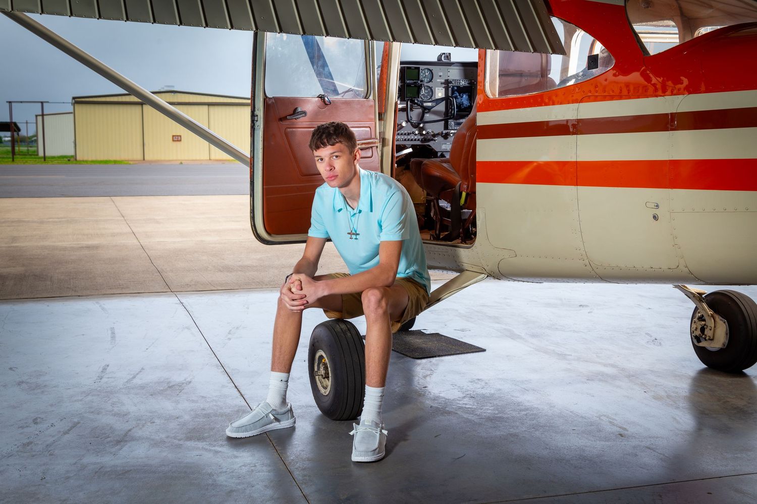 A person sits on the landing gear of a small aircraft with red and white stripes in an airplane hangar.
