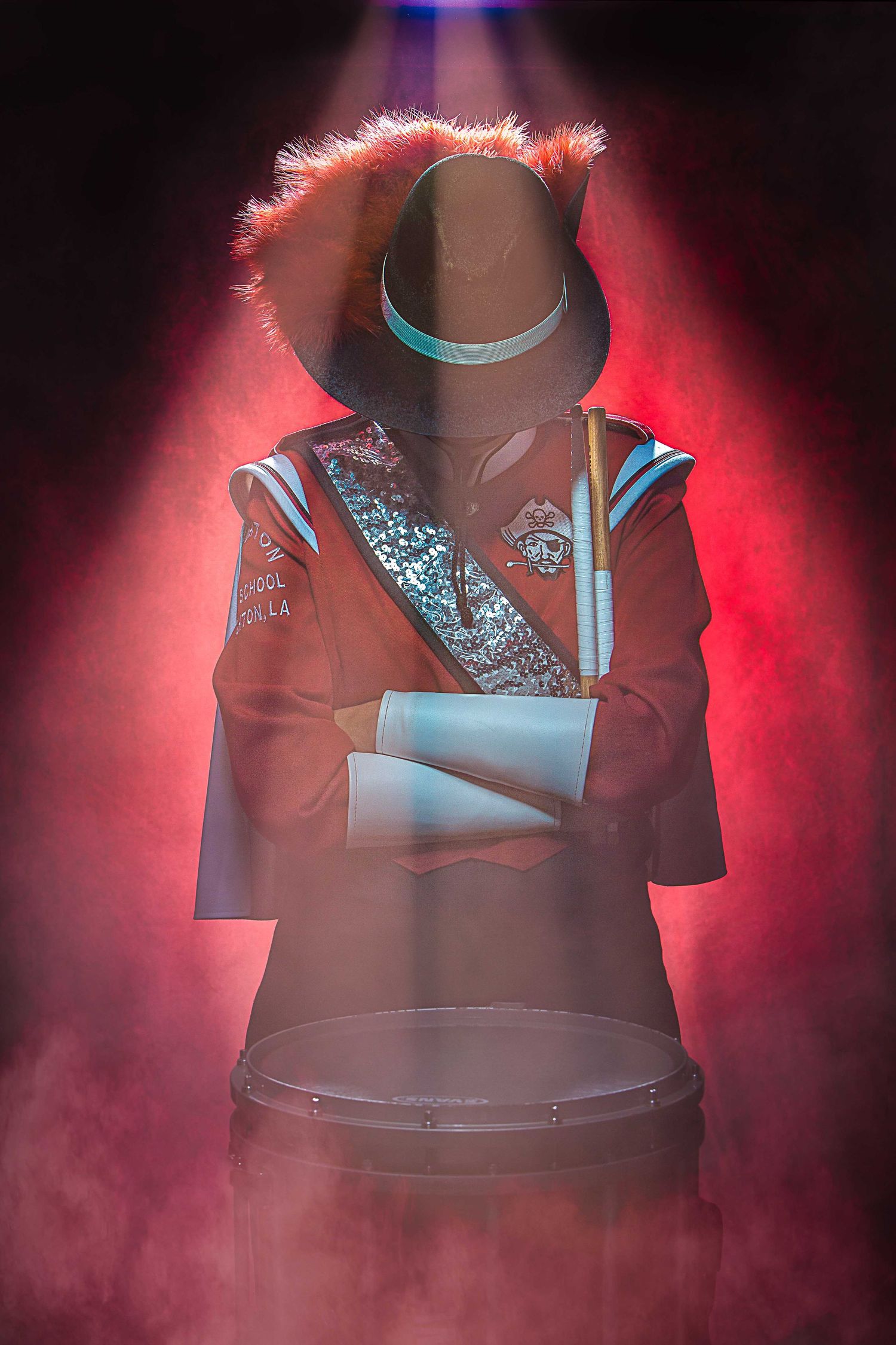 Dramatic portrait of a High School marching band member silhouette against red smoke with a brown hat and embellished band uniform.