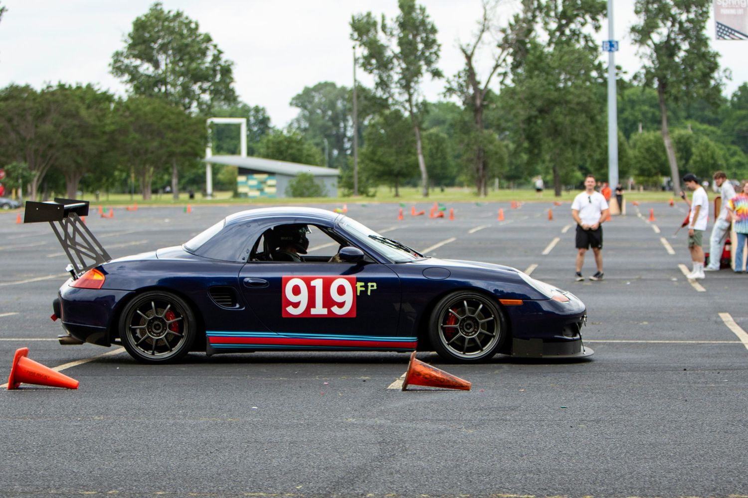 Dark blue Porsche 919 FP autocross race car navigating orange cone course in parking lot competition.