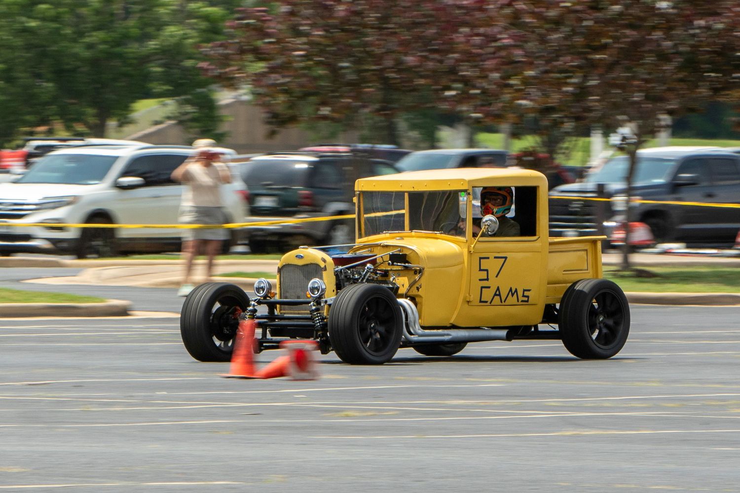 Yellow hot rod number 57 racing through orange cones in a sunny parking lot autocross event.