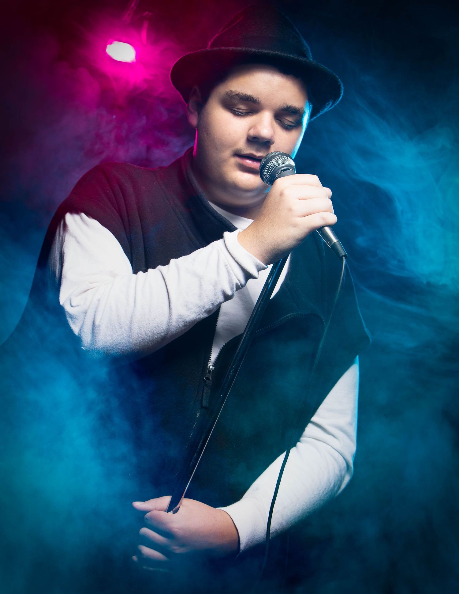 A musician performs in dramatic lighting with blue and pink smoke effects creating an atmospheric stage environment.
