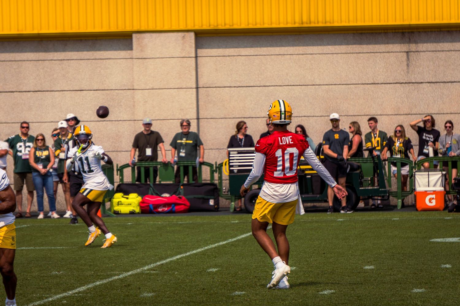 Football players in yellow and green uniforms compete on a field during a game with spectators watching from sidelines.