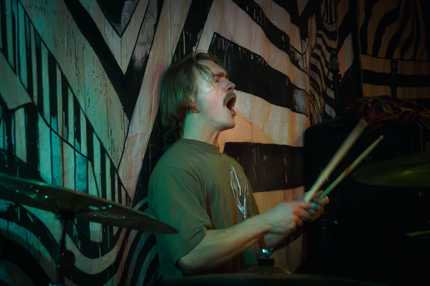 A series of dark atmospheric photos showing a drummer performing in a dimly lit venue with green lighting.