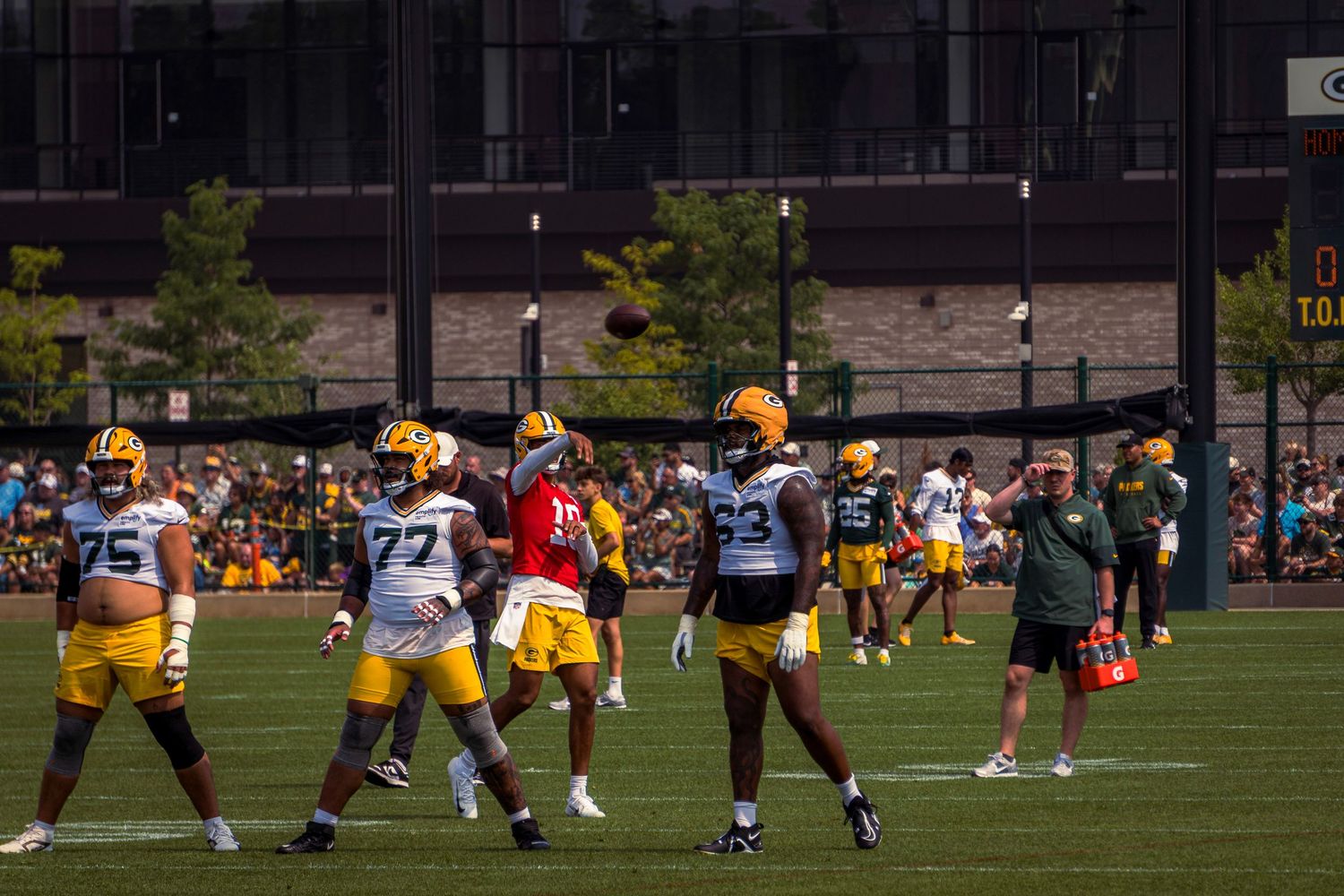 Football players in yellow and white uniforms line up on the practice field during a training session.