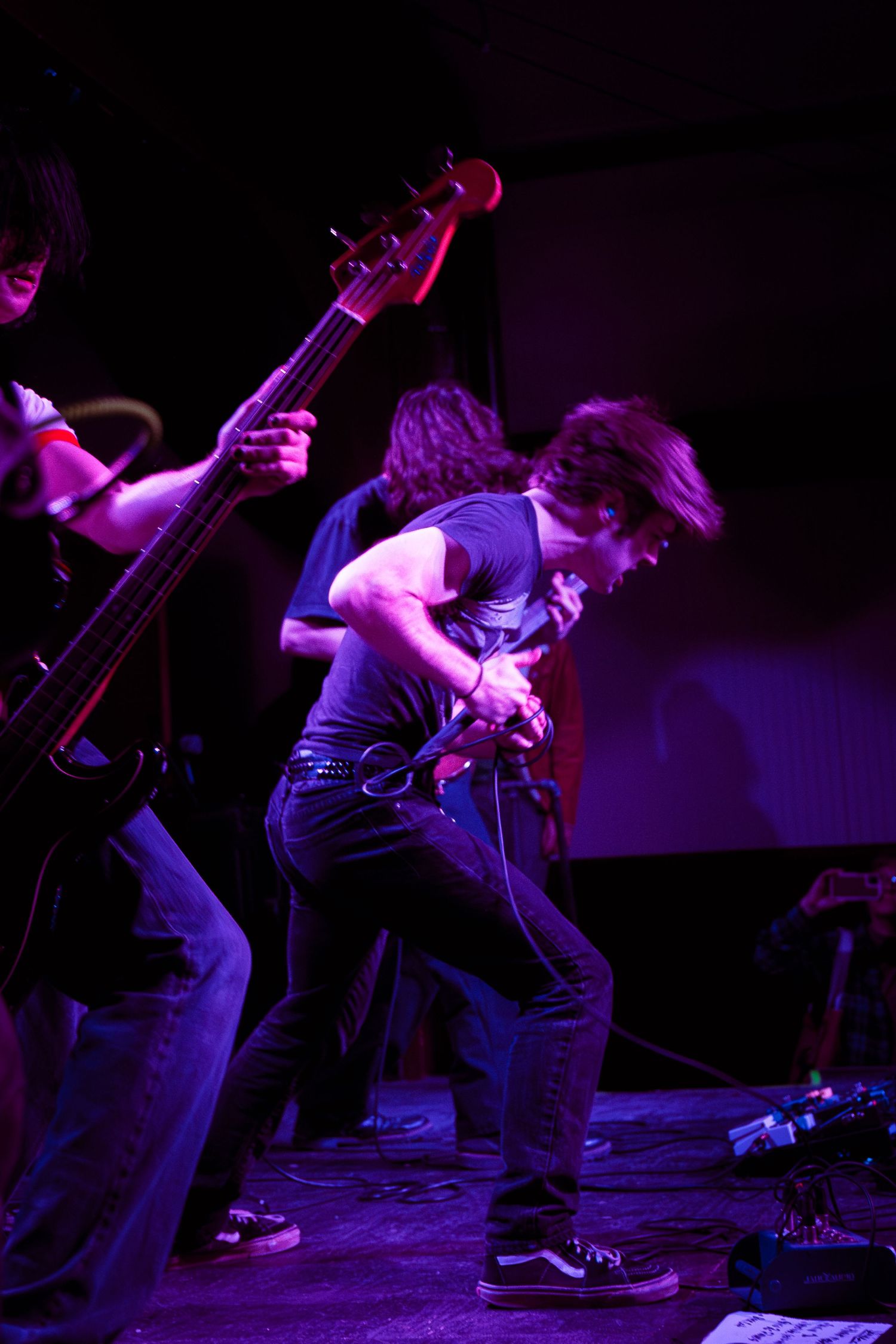 A performer crouches on stage bathed in purple lighting during an energetic live music performance.