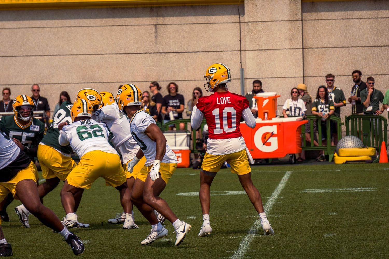 Football players in green and yellow uniforms line up at the line of scrimmage during a game with spectators watching.