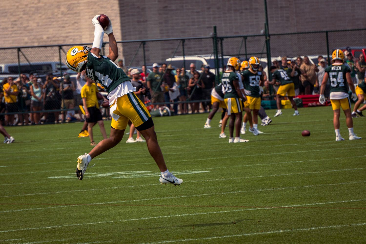 Football players in yellow and white uniforms practice drills during a training session on a grass field.