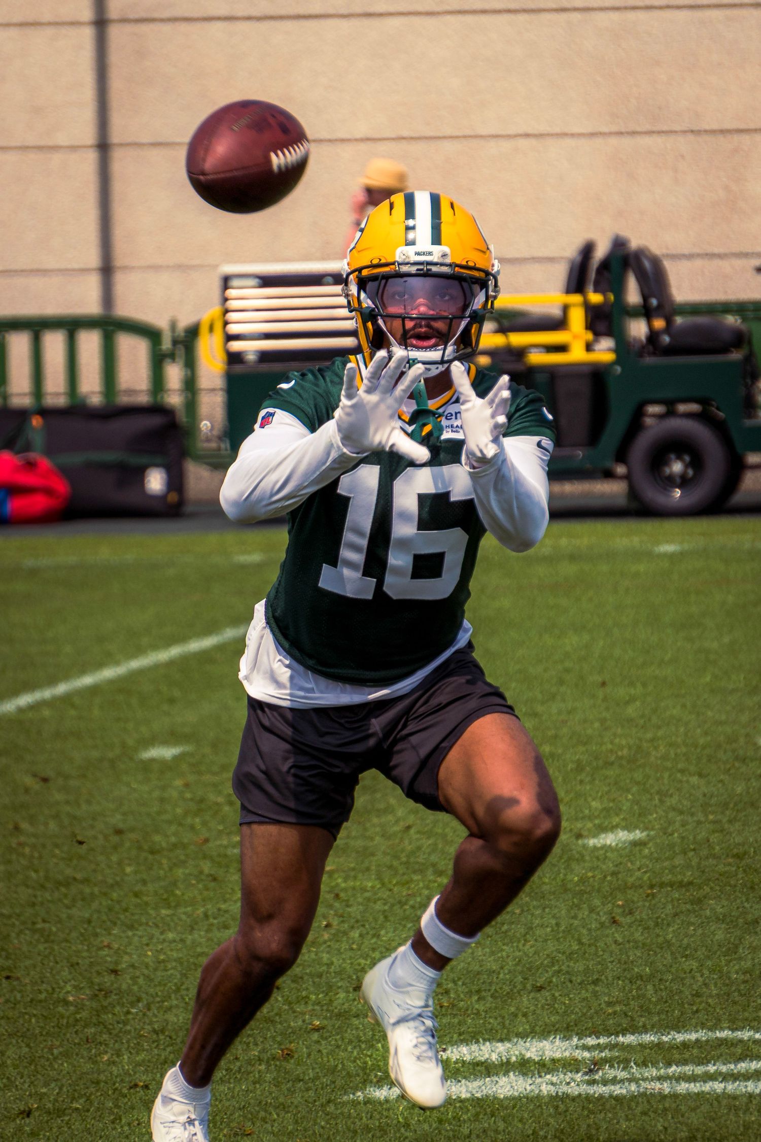 Football player catches ball during practice drill on outdoor field with yellow equipment visible in background.