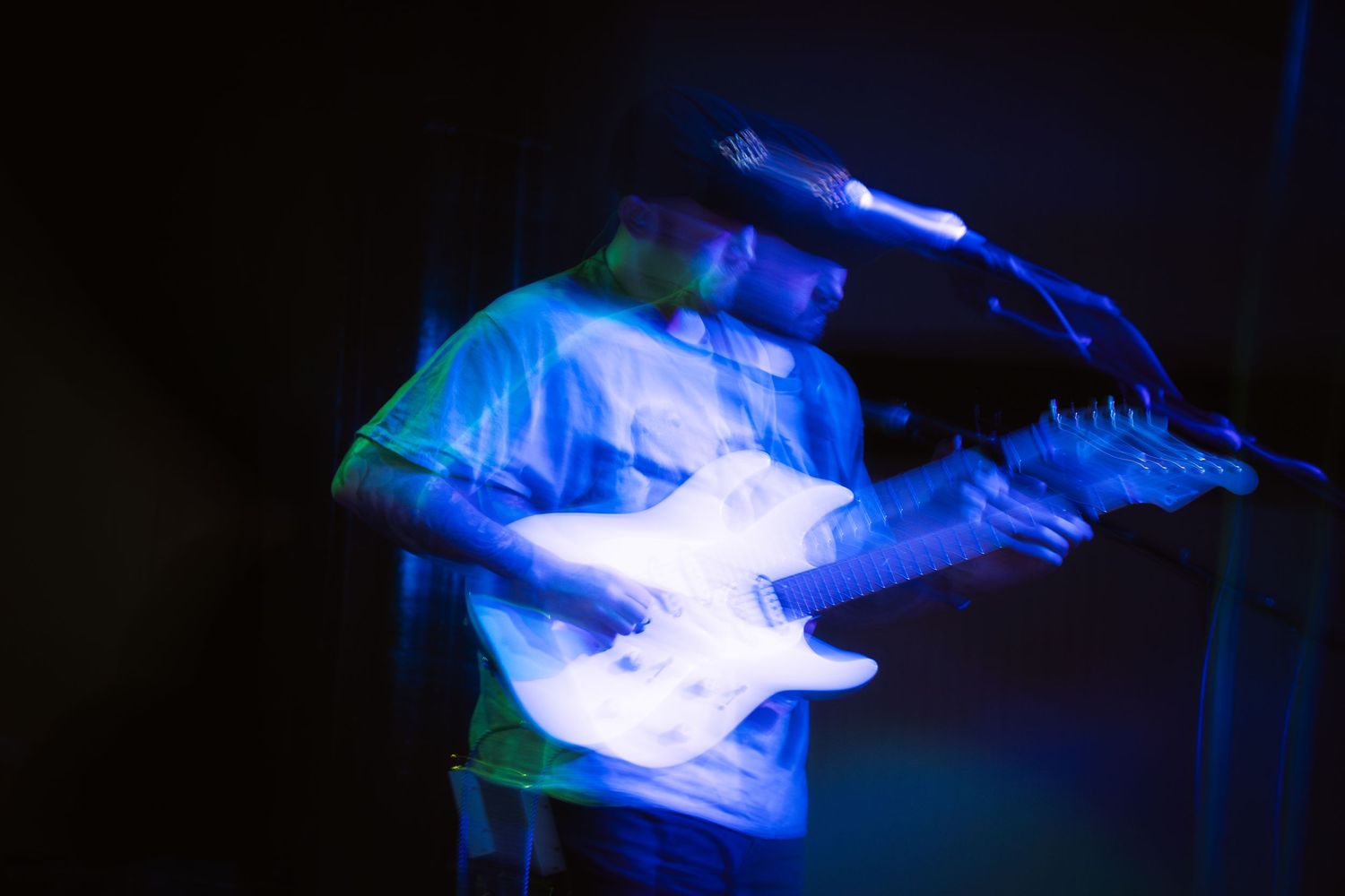 A guitarist performs on stage illuminated by dramatic blue lighting while playing an electric guitar.