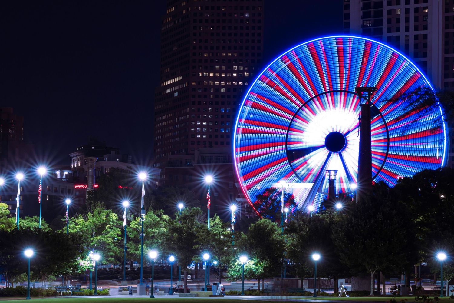 A colorful Ferris wheel illuminates the night sky with red and blue lights against a cityscape backdrop.