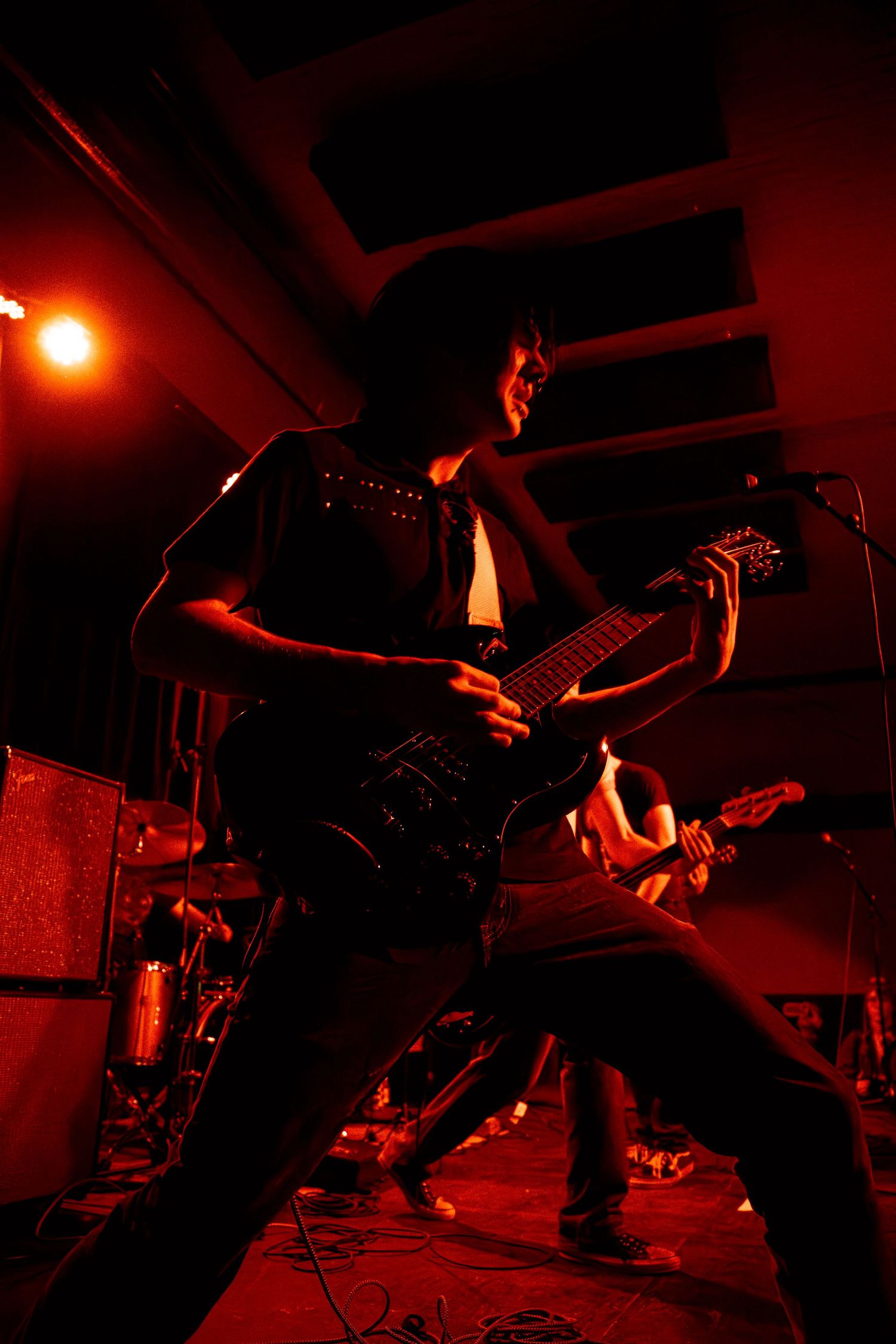 Band members perform on stage in dramatic red lighting during an energetic rock concert performance.