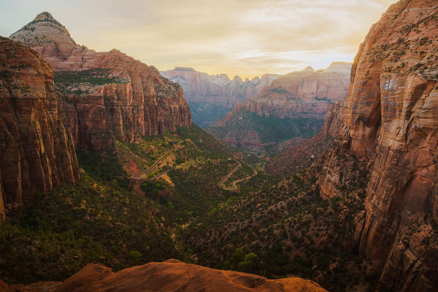 Aerial view of Zion Canyon's red rock cliffs and lush green valley at golden sunset in Zion National Park, Utah.