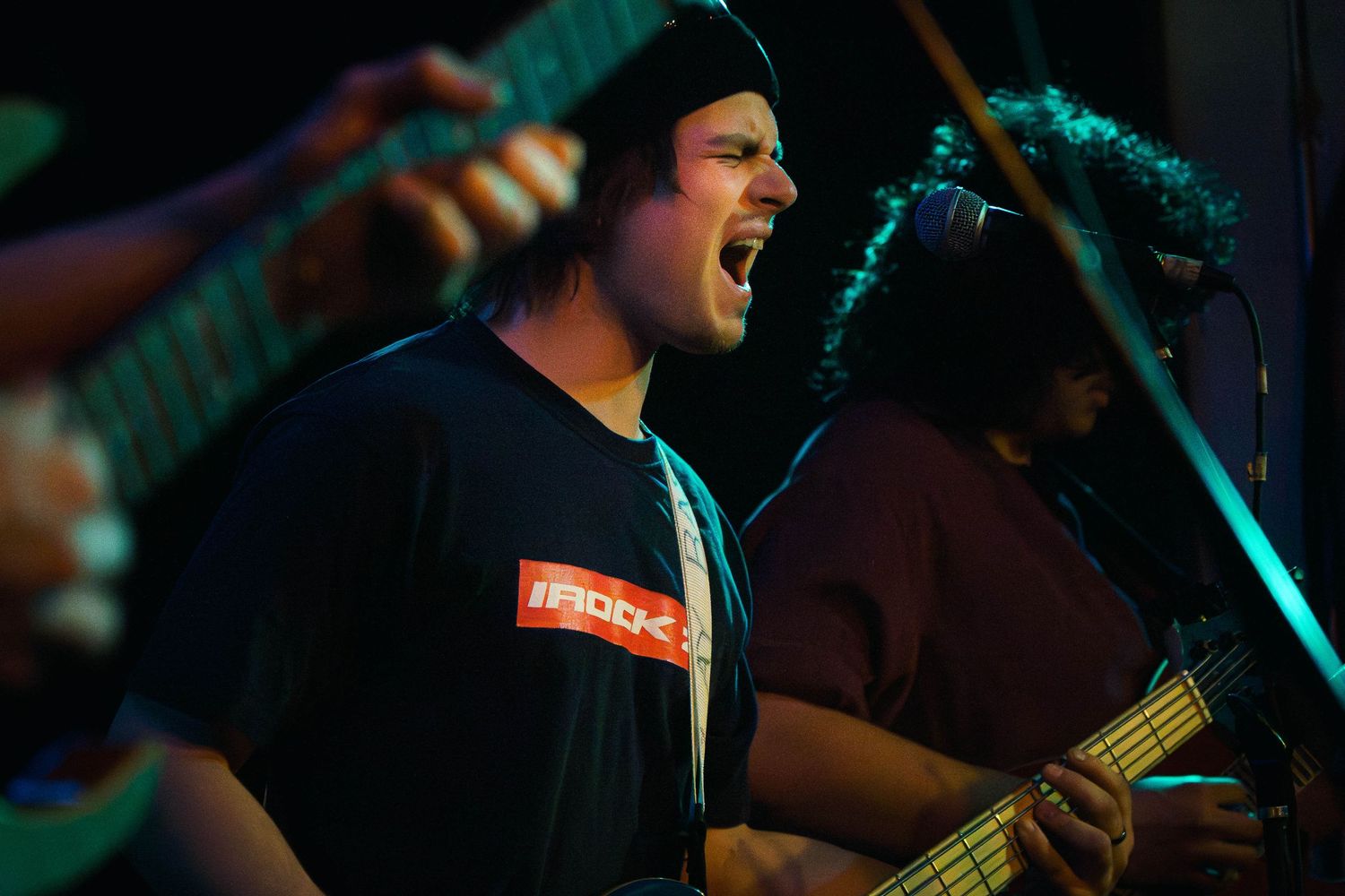 A musician performs on stage with dramatic blue lighting and a microphone stand during a live concert performance.