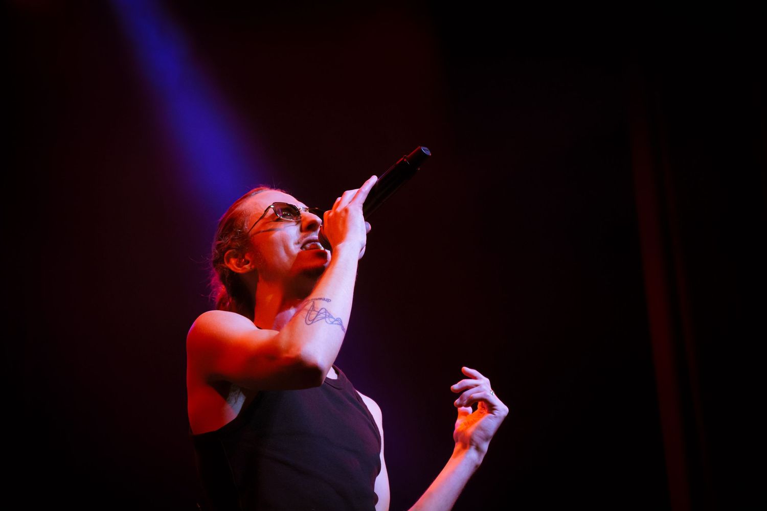 Performer sings emotionally into microphone under dramatic red stage lighting at live concert venue.