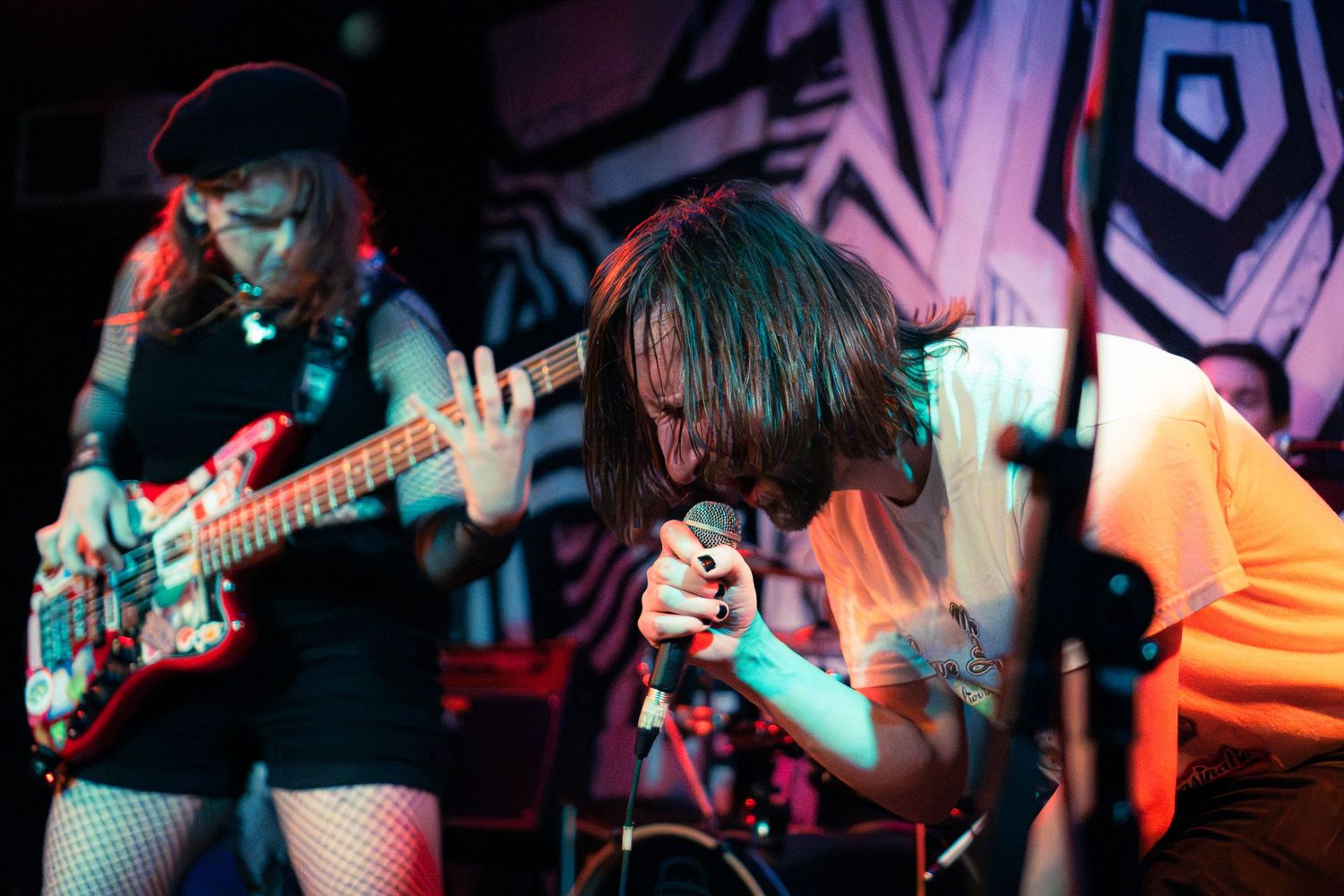 Concert performers play guitars on stage with colorful pink and blue lighting effects in the background.