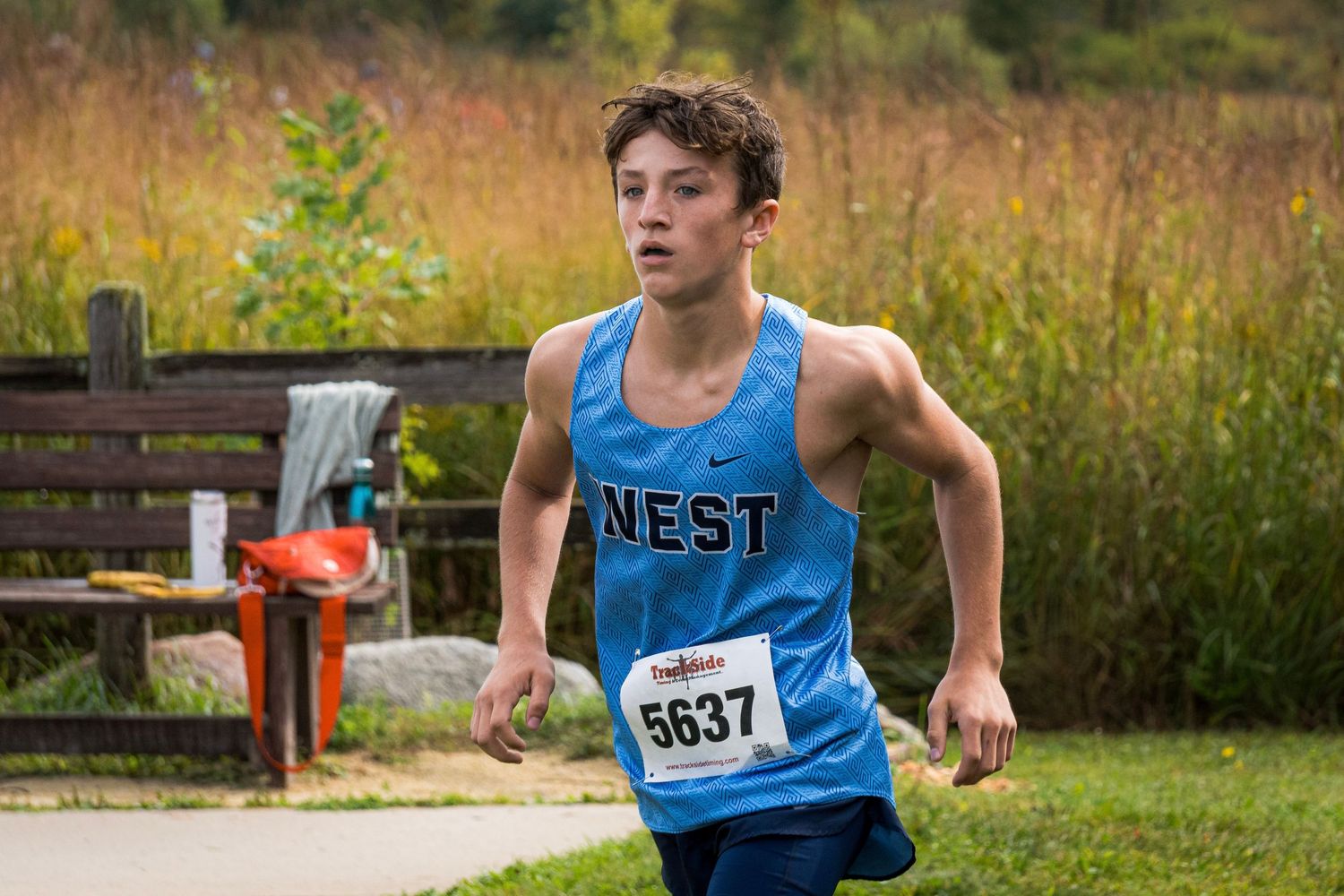 Runner in blue singlet participates in cross country race through grassy outdoor course.