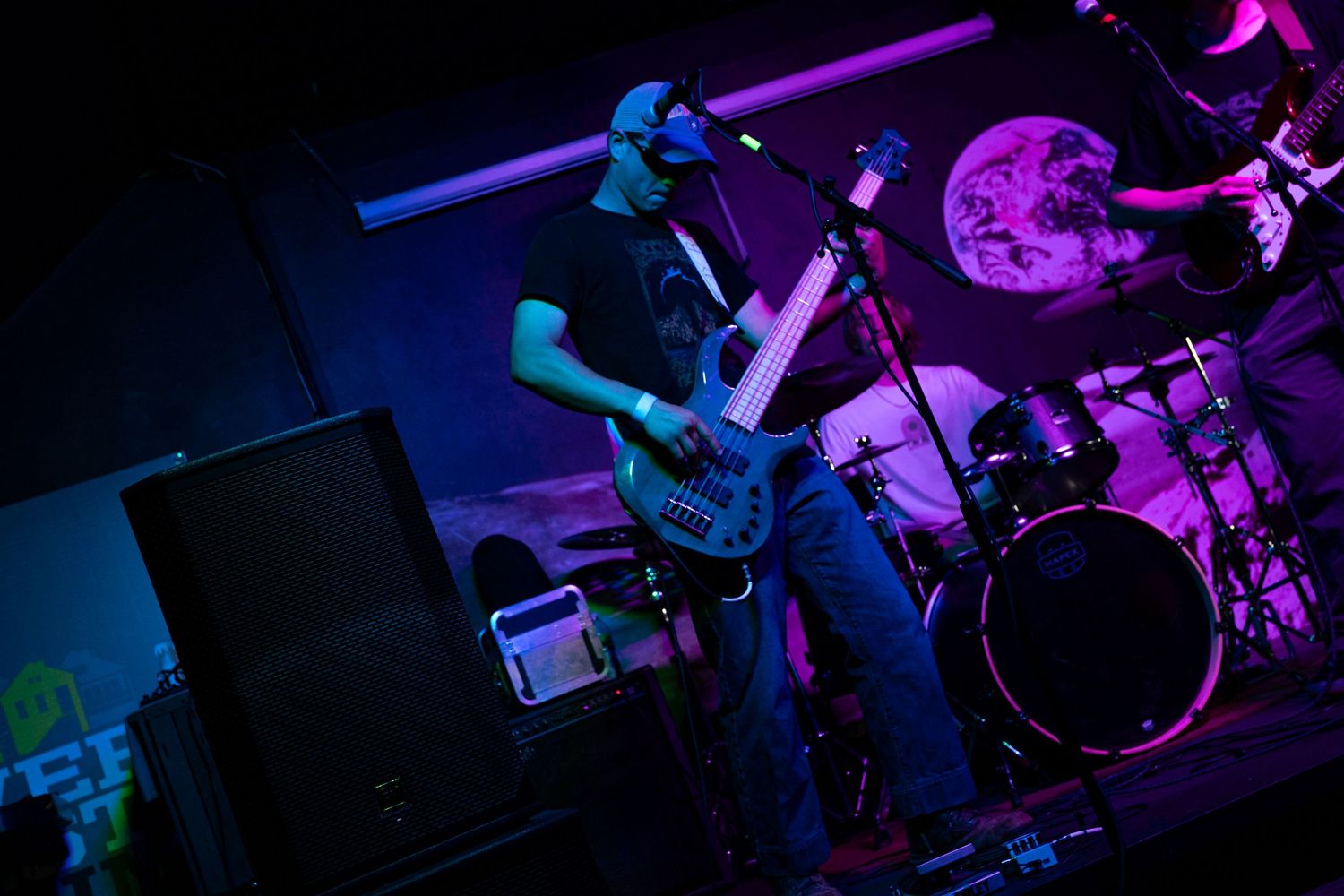 Concert performers on stage bathed in vibrant purple and blue lighting during a live music performance.