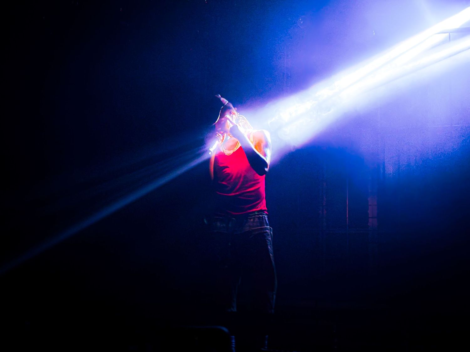A performer in a glowing red costume dances gracefully against a dark background illuminated by bright blue spotlights.