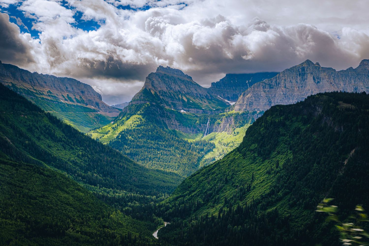 Sweeping mountain valley vista with lush green slopes and dramatic cloud formations over rugged peaks.
