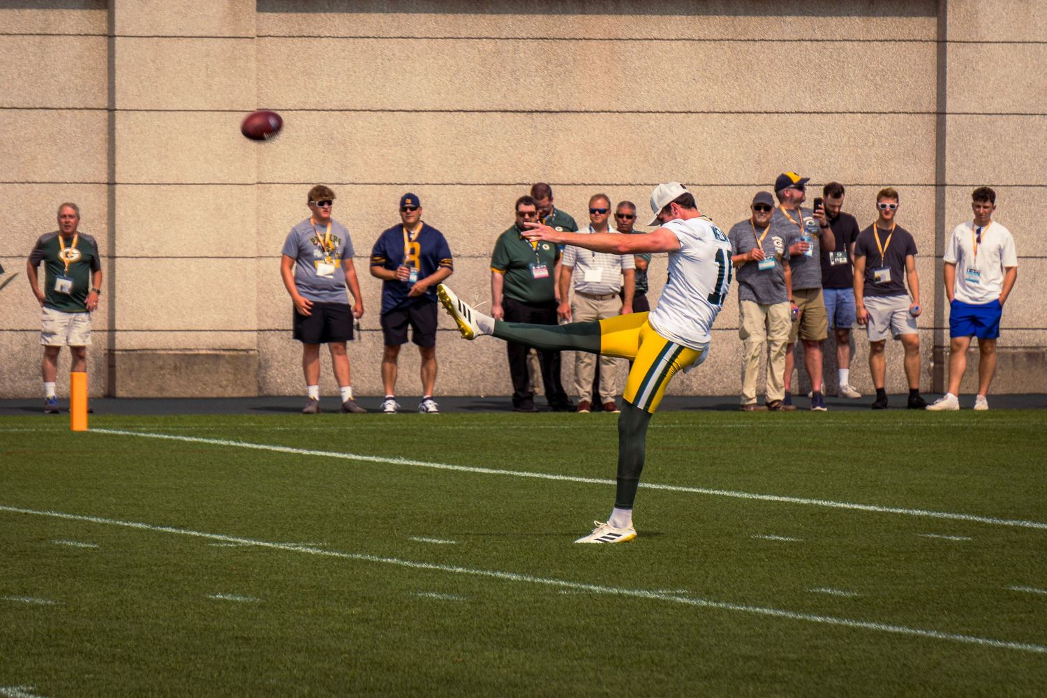 A football soars through the air towards goal posts during a practice session on a grass field.