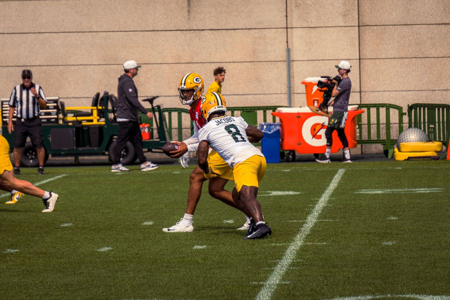 Football players in yellow and white uniforms compete during a game with officials and sideline equipment visible.
