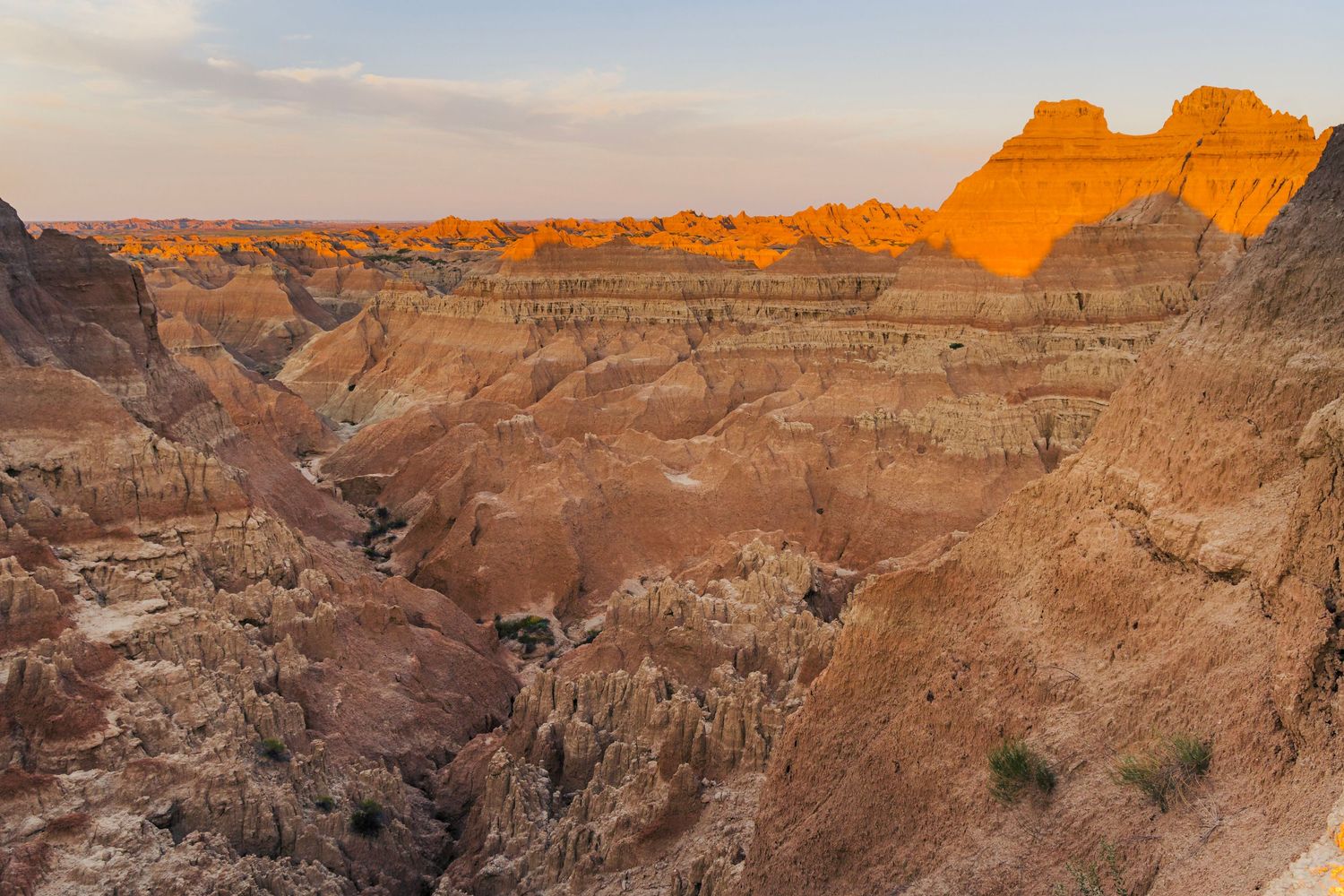 Rugged canyon landscape in Badlands National Park glows orange at sunset with layered rock formations and deep ravines.