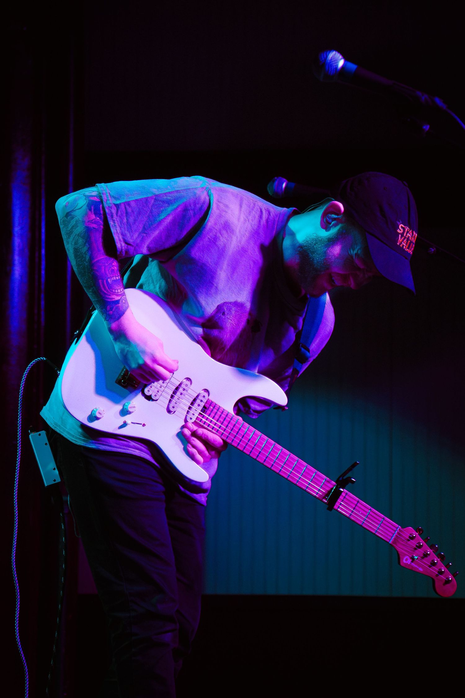 Electric guitar performance under dramatic purple and blue stage lighting creates moody atmospheric effect.