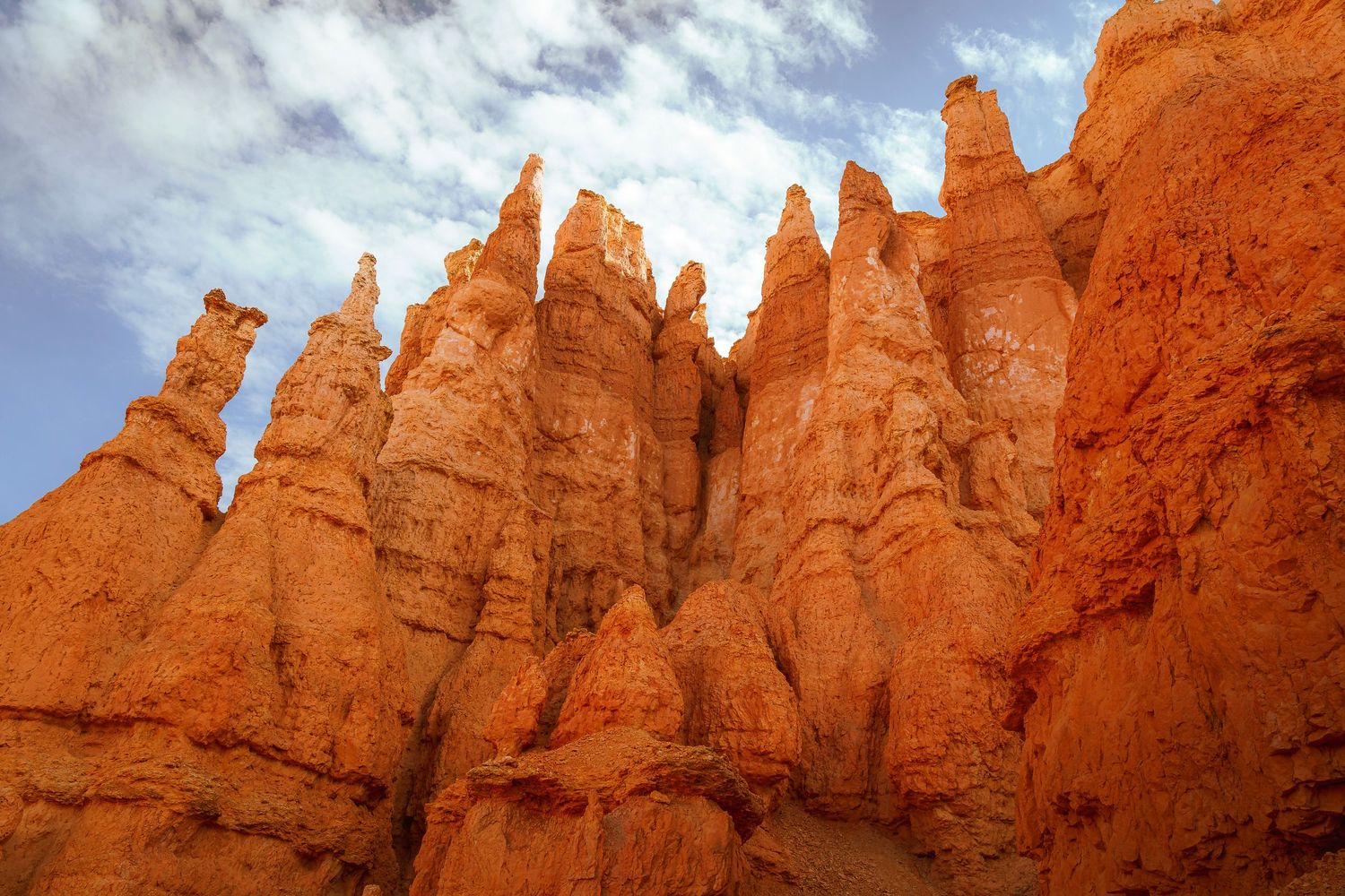 Towering orange hoodoo rock formations at Bryce Canyon National Park against a partly cloudy blue sky.