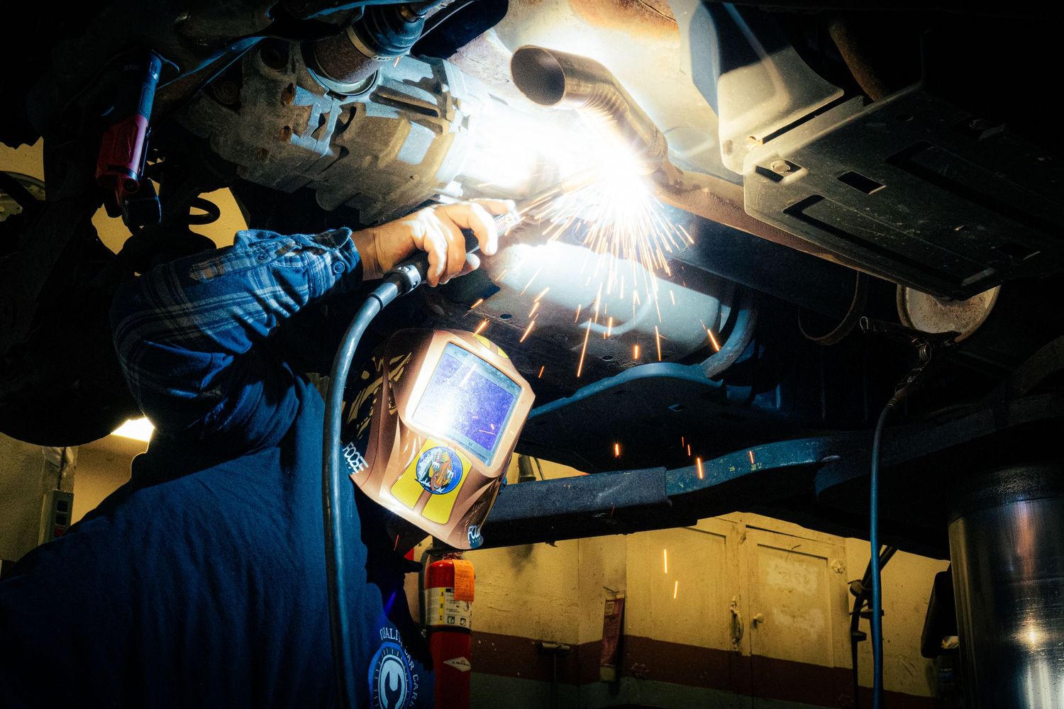 Welder working with protective equipment creates bright sparks while performing metal fabrication in industrial setting.
