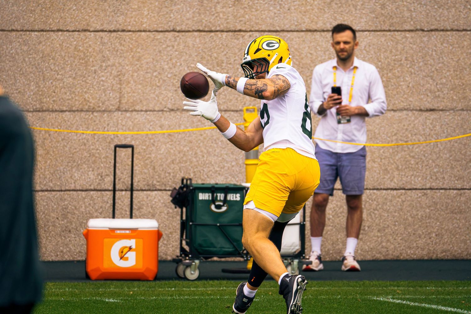 Green Bay Packers player catches a football during an indoor practice session at training facility.
