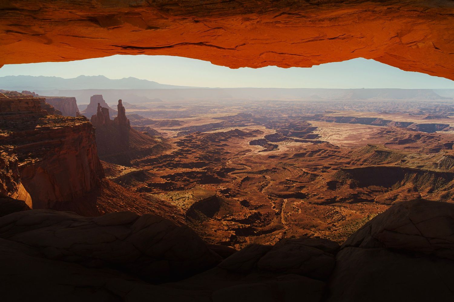 Panoramic view of Canyonlands National Park through a sandstone arch, showcasing vast red rock formations.