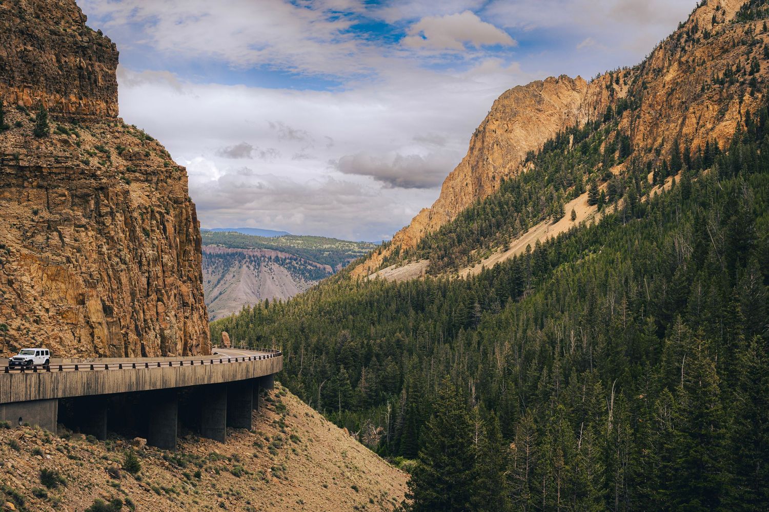 A panoramic view of towering rocky cliffs and mountains in Yosemite National Park under a cloudy blue sky.