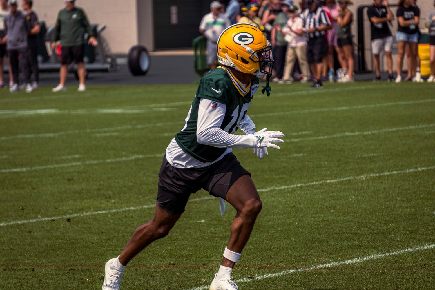 Green Bay Packers players practice offensive drills during training camp on a sunny football field.