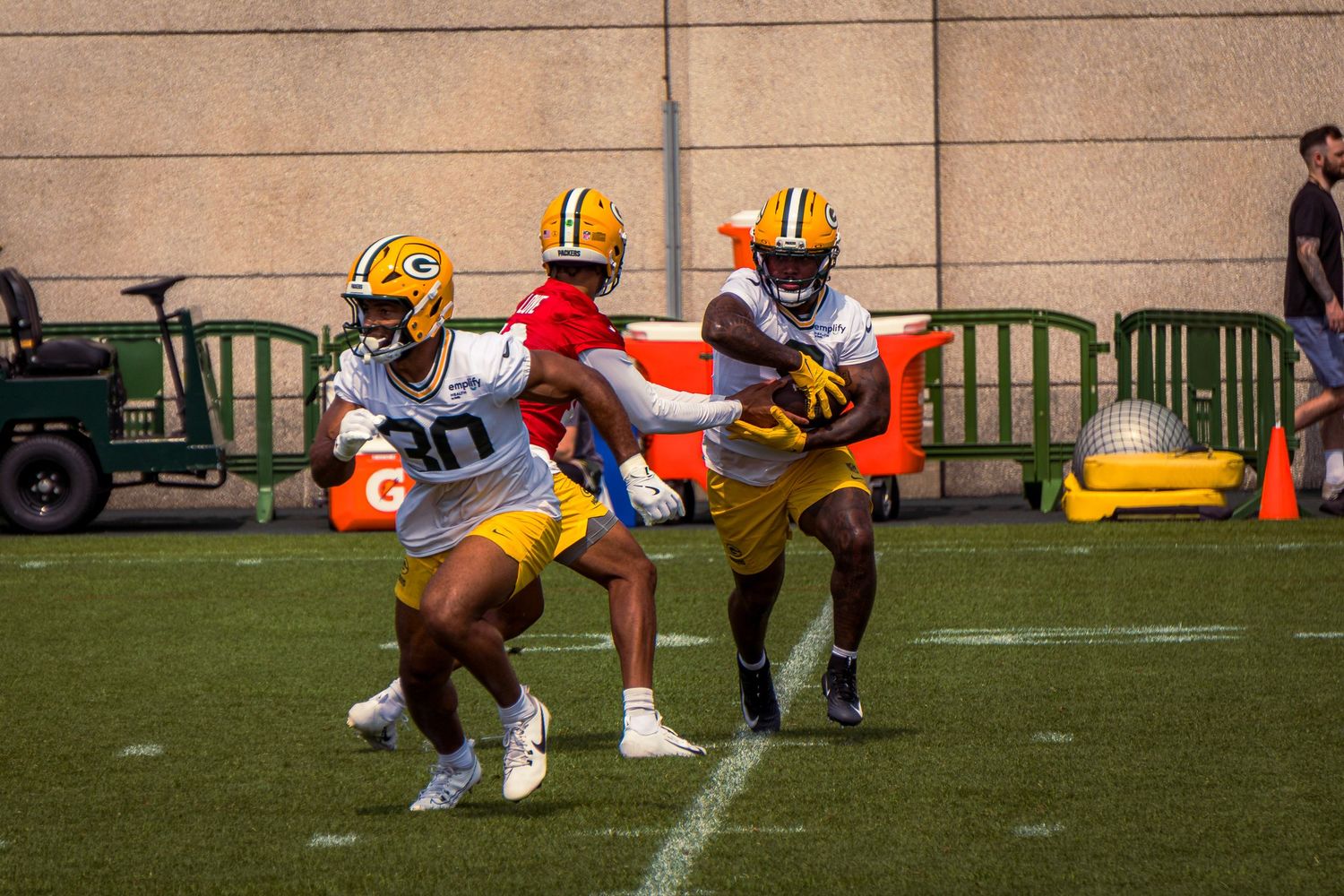 Green Bay Packers players practice football drills on a grass field during training camp.